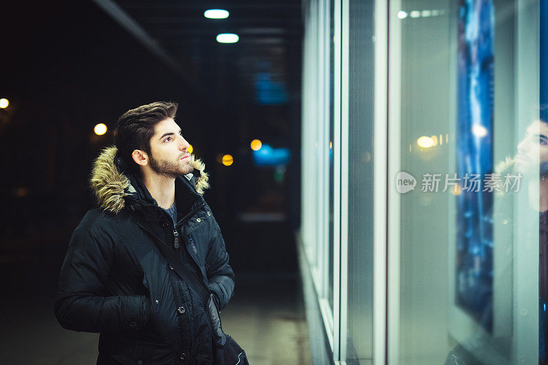 年轻人走在晚上，看着城市商店的橱窗