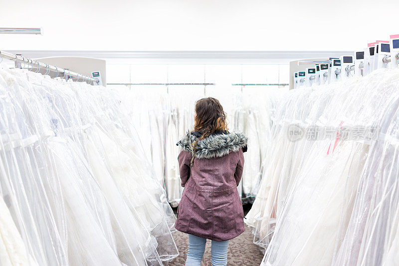 年轻女子在精品店的折扣店选购婚纱，许多白色服装挂在衣架排
