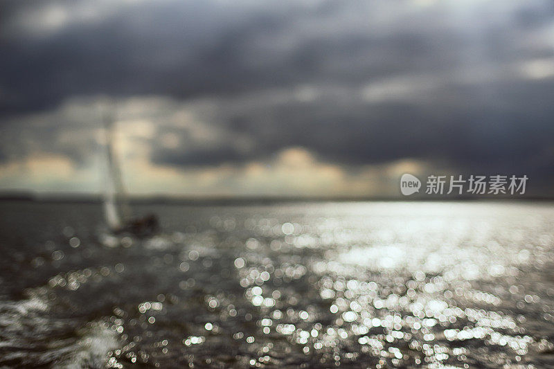 帆船在水面上，戏剧性的云和阳光失去焦点