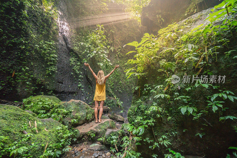 在巴厘岛的热带雨林中，旅行的年轻女子张开双臂拥抱大自然的美丽。人们以自然为旅游理念。