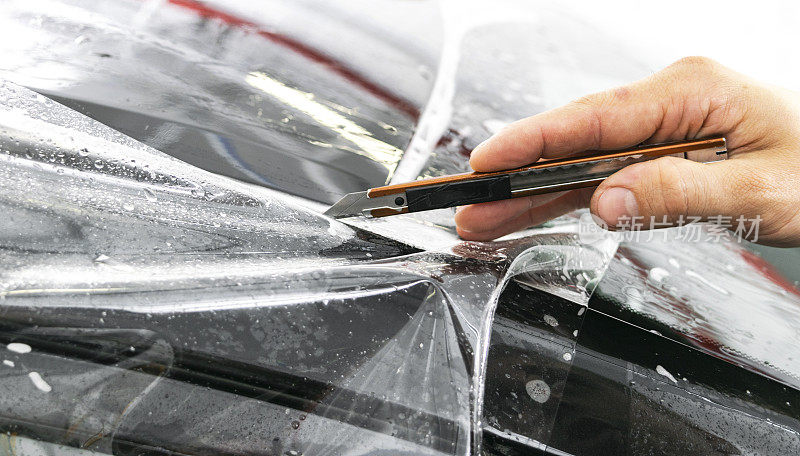 汽车包装专家将乙烯基箔或薄膜放在汽车上。保护膜。用工作工具涂保护膜。汽车详细。透明薄膜。车漆保护。修剪。