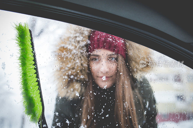 年轻女子正在清理车窗上的雪