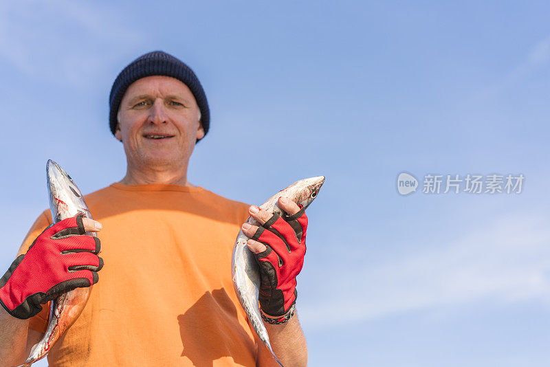 休闲渔民幸福与两只鱼在他的手对着蓝天而航行在亚得里亚海海岸。