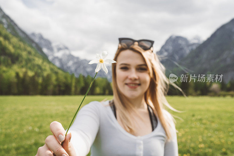 一个金发碧眼的小女孩戴着太阳镜在草地上采摘水仙花