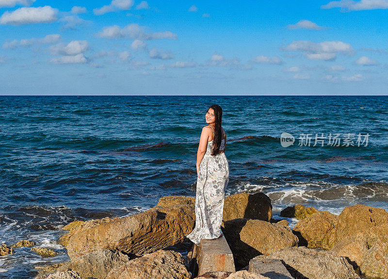 年轻漂亮的泰国裔柬埔寨裔美国妇女站在海边一块露出海面的岩石上