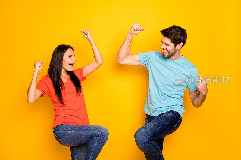 搞笑的两个人的照片，男人女士庆祝最喜欢的足球队获胜，举起拳头，高兴穿休闲的蓝色橙色t恤牛仔裤孤立的黄色背景