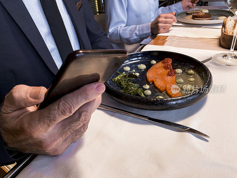 在餐厅吃午餐时使用智能手机。桌上有一盘海鲜