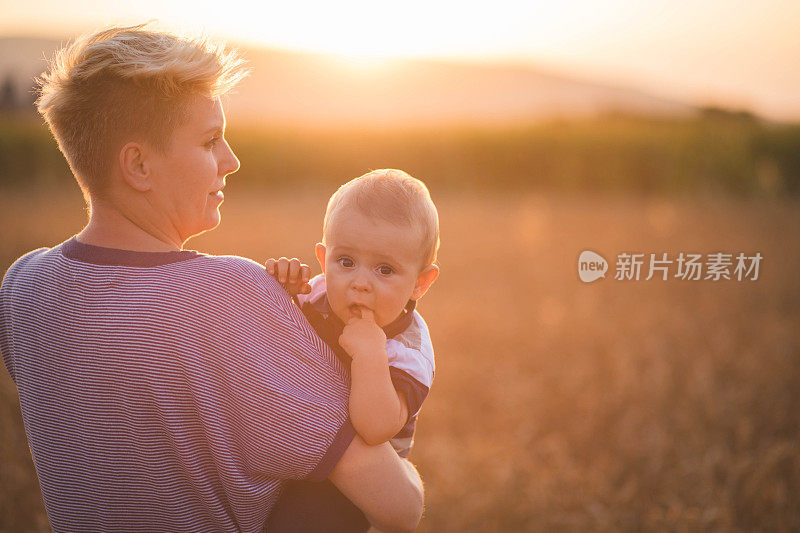 女人抱着孩子在金黄的麦穗地里种庄稼。