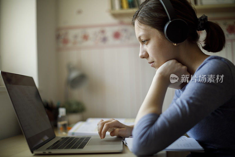 十几岁的女孩戴着耳机在家里用笔记本电脑学习