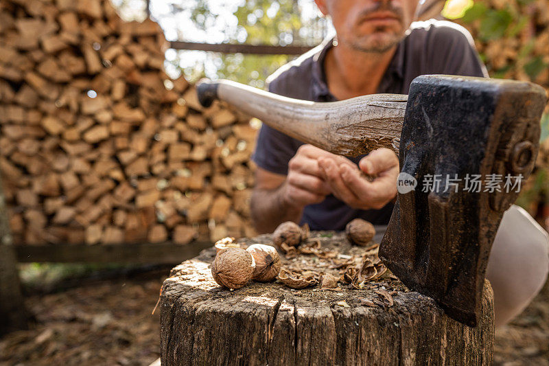 男人蹲在木头后面吃着核桃，后面的斧头被卡在一块木头里