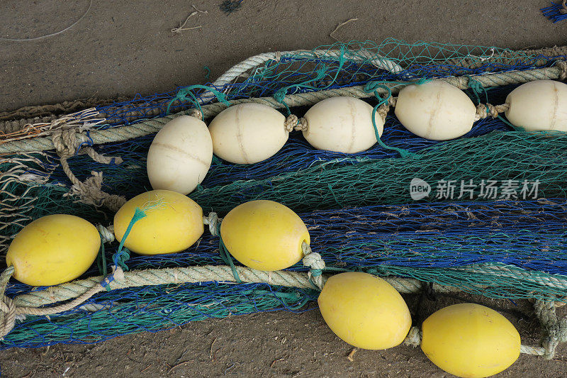 一串黄色和白色的漂浮物躺在蓝绿色的渔网上