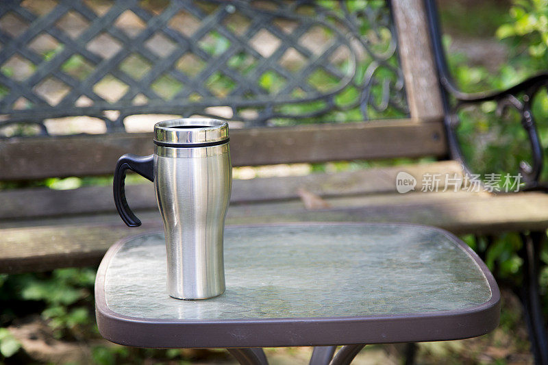 一个可重复使用的咖啡杯放在公园的桌子上。长椅上的背景。