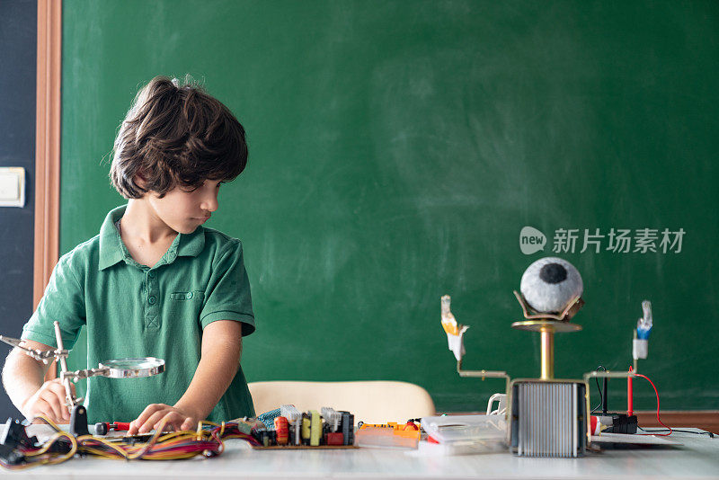 一个小学生在绿色黑板前研究机器人和编程