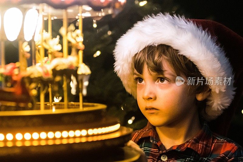 小男孩戴着圣诞老人的帽子看着玩具旋转木马