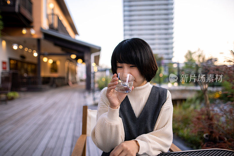 年轻女子在露天咖啡馆喝水