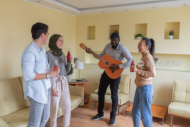 一群欢乐的不同种族的朋友在现代公寓里弹吉他跳舞。