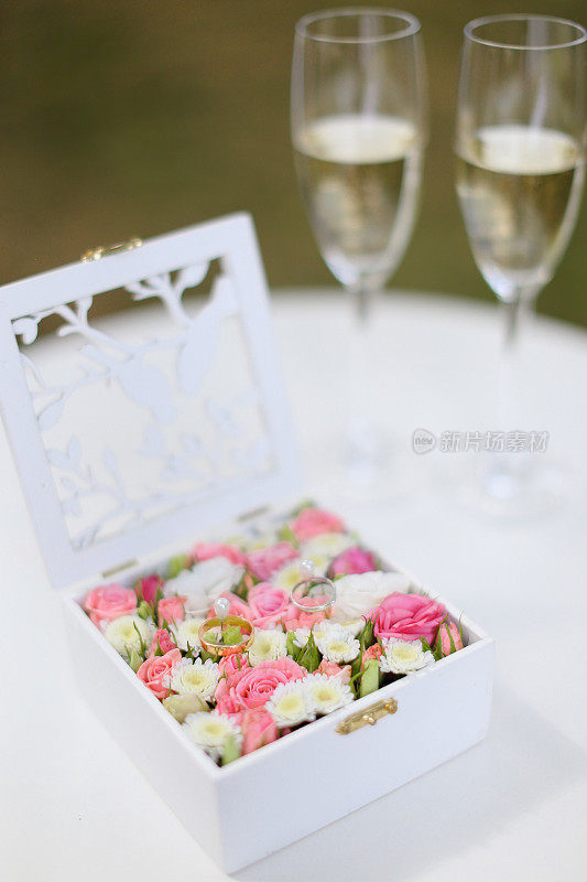 两个金戒指躺在花盒里，旁边是放着香槟的酒杯