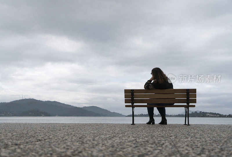 一个超重的年轻女人坐在海边的长椅上看风景