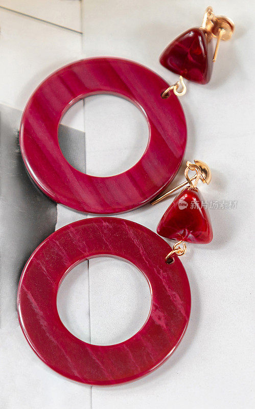 红耳环被放在卡片卡片上。红色的耳环上点缀着浅色的线条。耳环的形状是戒指，材料与石头非常相似。