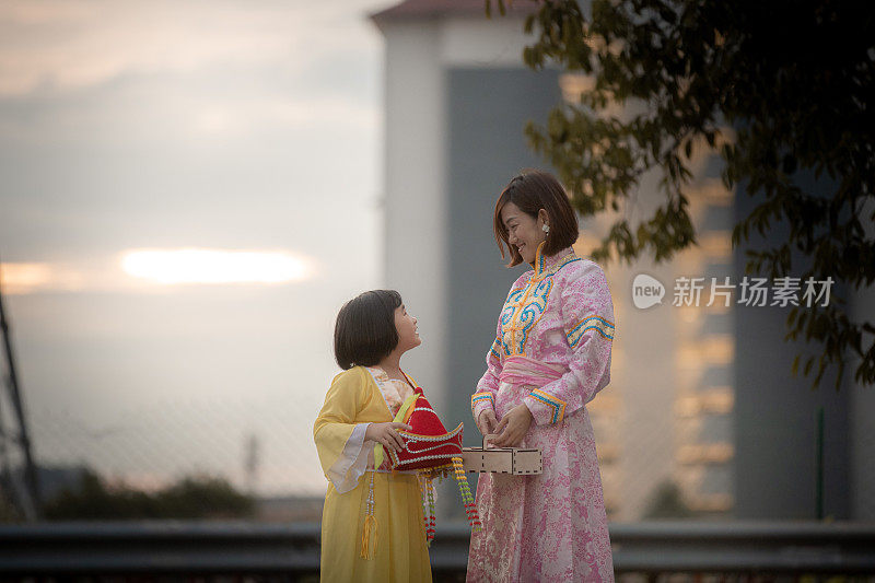 亚洲华人妈妈和女儿穿着传统服装，手拿月饼盒享受月饼节
