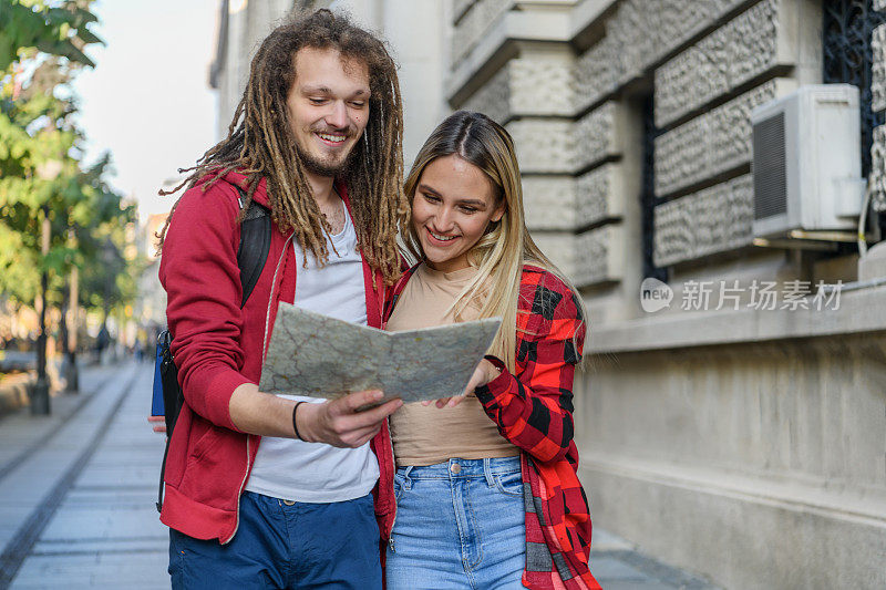 一个年轻人和他的女朋友带着旅游地图在市区散步。