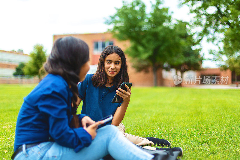 青春期前的女学生坐在校园草坪户外使用技术教育照片系列