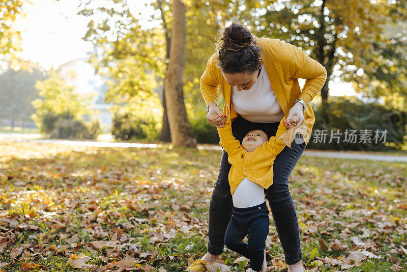 妈妈抱着她的宝贝女儿，害羞地试图在公园里迈出第一步