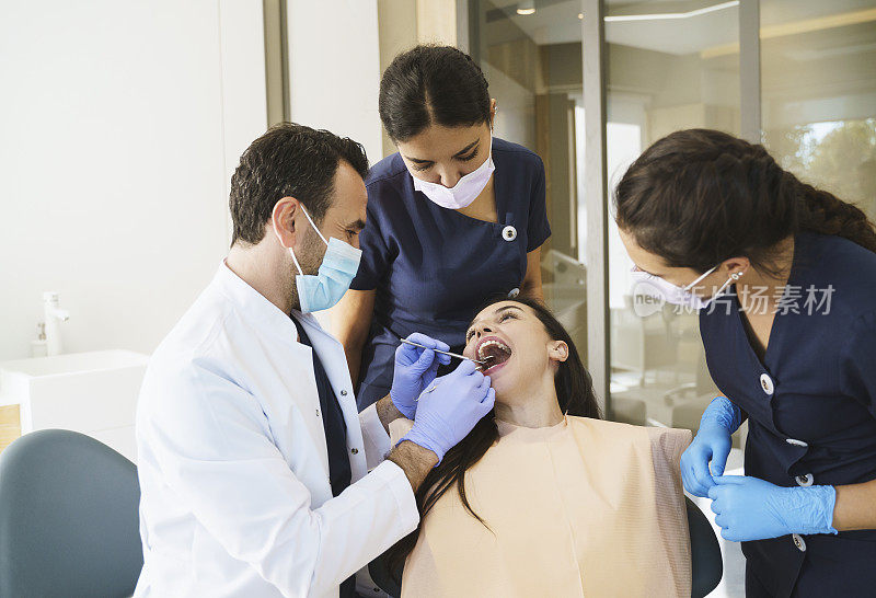 男牙医戴着手套和口罩，与牙科小组一起检查病人的牙齿