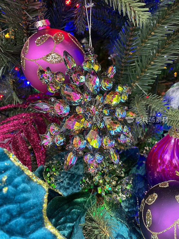 形象独立，水晶玻璃，彩虹色雪花饰品挂在人造圣诞树树枝上，云杉针，模糊的多色神仙灯背景