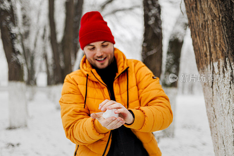 年轻英俊的男子在冬天的一天里，穿着暖和的衣服扔雪球