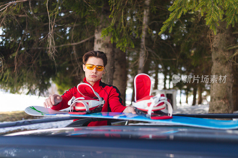 一个英俊的年轻人在树林里把滑雪板从车顶上拿下来