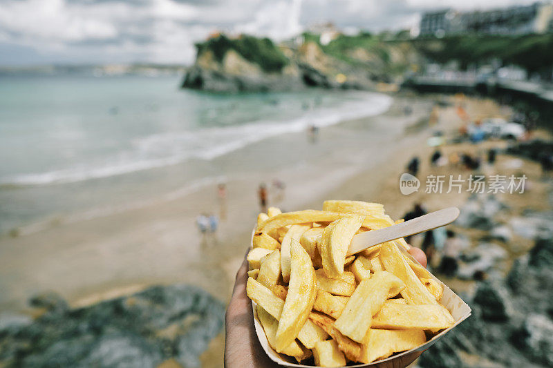 6月一个阳光明媚的日子，在康沃尔郡纽基镇海滩，一只手拿着一盒薯片。