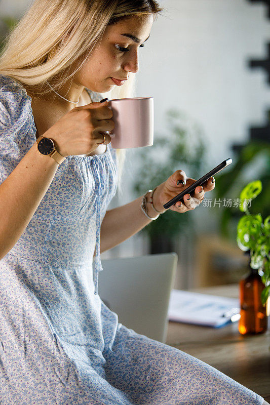 年轻的女商人一边喝咖啡休息，一边用智能手机回复短信