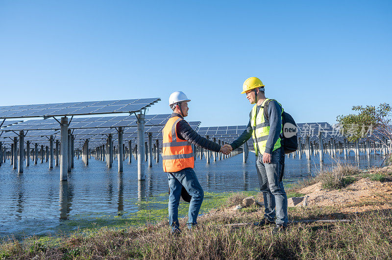 两名男工人在海边太阳能发电站前握手
