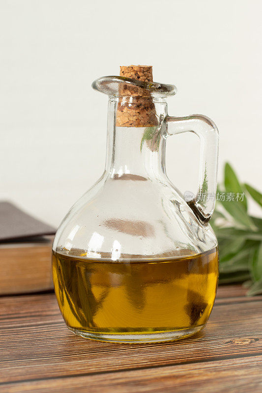 玻璃瓶里的纯橄榄油，一本合上的《圣经》，白色底色的木桌上放着一根绿色的橄榄枝