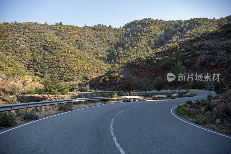 山路紧抱着陡峭的山坡，蜿蜒曲折，火山地形繁盛，傍晚的阳光洒在绿树成荫的山坡上