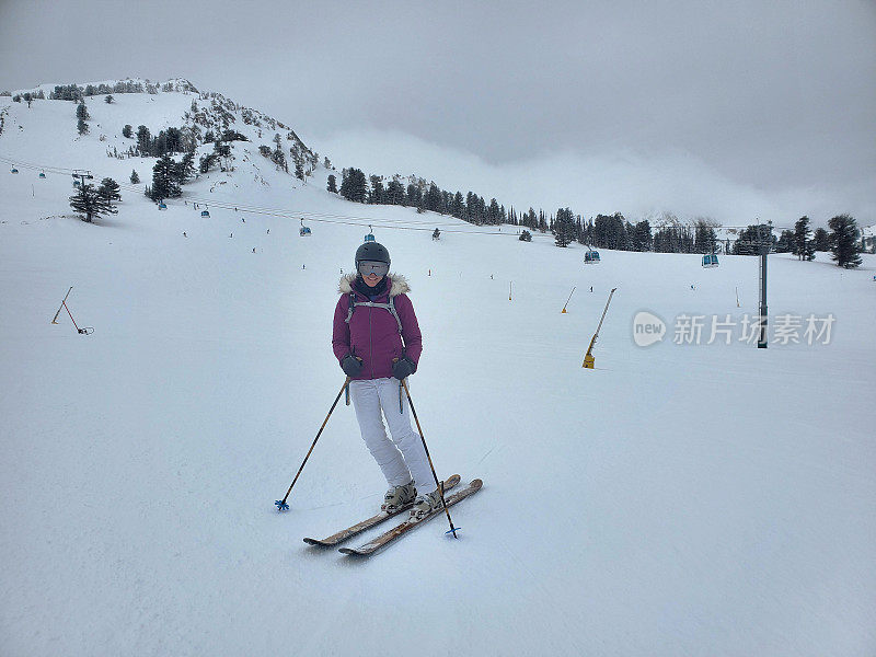 成熟的女子滑雪者在雪盆滑雪场的山坡上，犹他州在一个多云多雾的日子。背景是草莓贡多拉。