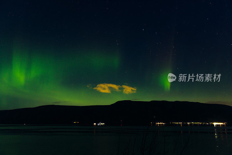 风景秀丽的北极光在峡湾和发光的城镇在挪威