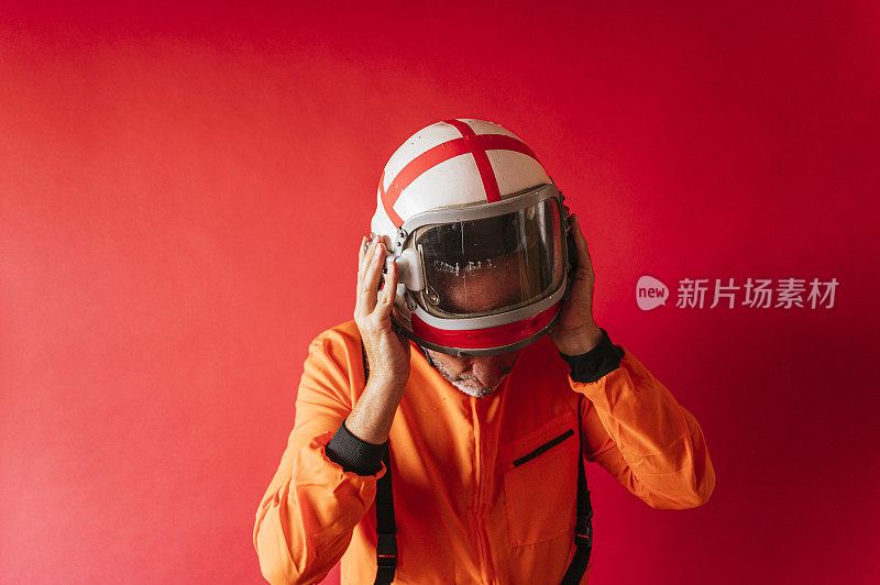 身着橙色太空服的宇航员在红色背景下摘下头盔