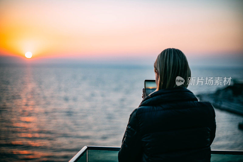 一名女子用智能手机在海滩上拍摄日落
