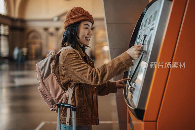 一名年轻漂亮的中国女子在巴塞罗那地铁站使用自动取款机取钱购物