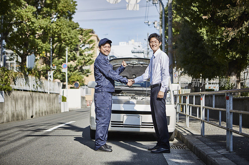 两个人在一辆车前握手，面带微笑地看着对方