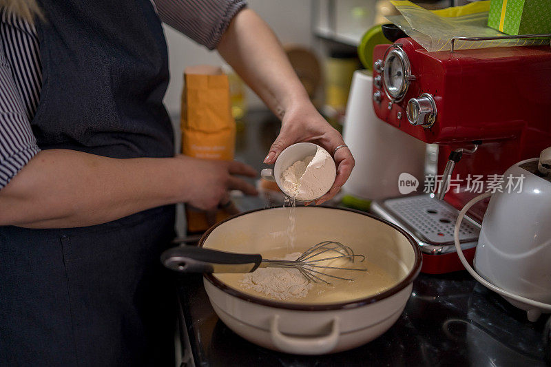 女厨师将一杯面粉倒入搅拌碗中。烘焙饼干的概念