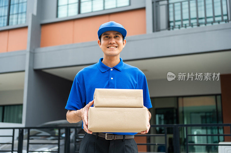 亚洲快递员手里拿着包裹，穿着蓝色制服，把包裹从网上购物送到顾客家门口，服务周到。快递员把包裹送到目的地。