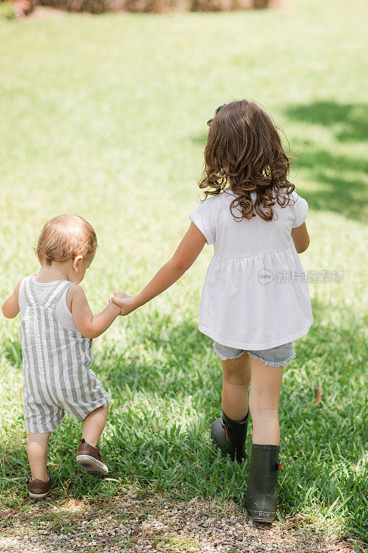 生活方式一对年轻的兄弟姐妹在佛罗里达州花园的西棕榈滩牵手散步，穿着鼠尾草绿和白色休闲夏装，古巴裔美国人4岁的蹒跚学步的女孩和1岁的男婴都是棕色头发