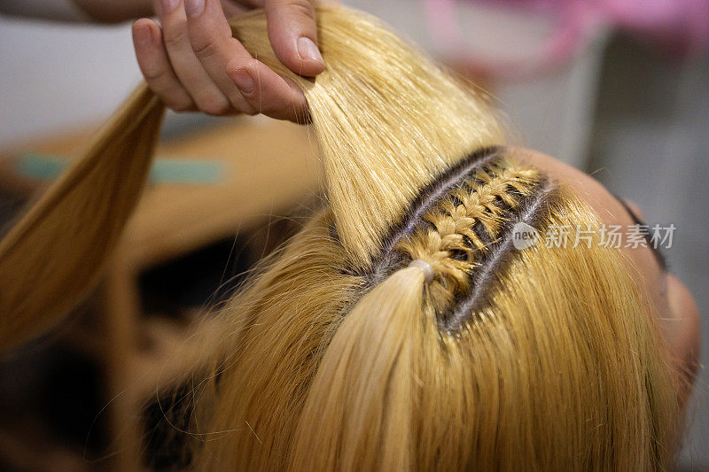 发型师在家工作，为她美丽的客户卷头发、编织小辫和马尾