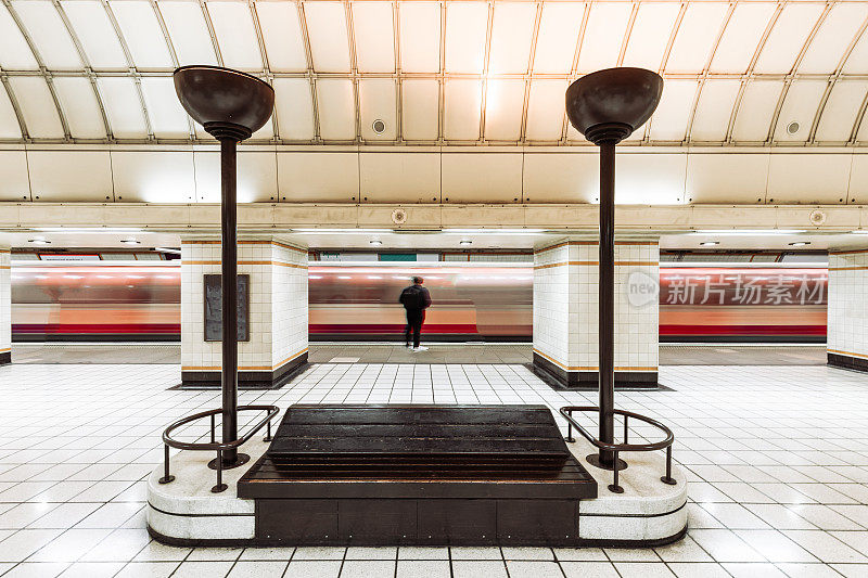 一名男子在城市的地铁站站台上等待着火车飞驰而过的模糊画面