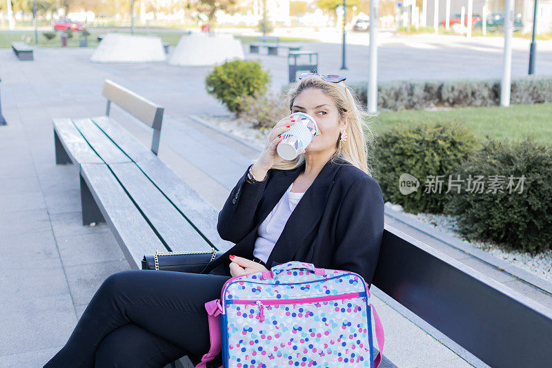 一位微笑的女商人在公园的长椅上休息，喝咖啡。