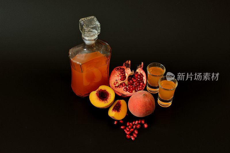 石榴桃利口酒，黑色背景的两杯和一瓶自制酒，附近有成熟的水果。