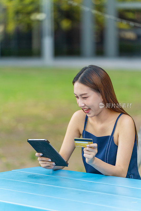 年轻的亚洲女性在户外公园用平板电脑进行数字银行信用卡交易